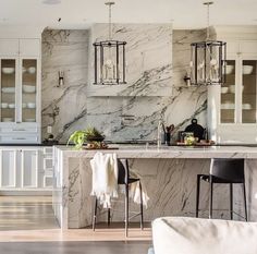 a large kitchen with marble counter tops and white cabinets, along with two bar stools