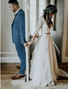 a man and woman standing next to each other in front of an open door wearing wedding dresses