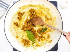 a wooden spoon in a white pan filled with ground meat and spices on top of a stove