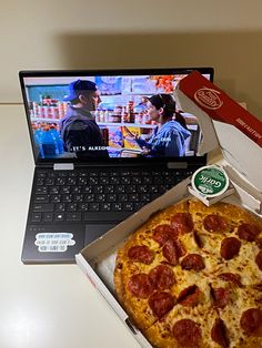 a pizza sitting in front of a laptop computer on a white table with a slice of pizza next to it