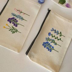 two embroidered tea towels with flowers on them next to a bottle of water and scissors