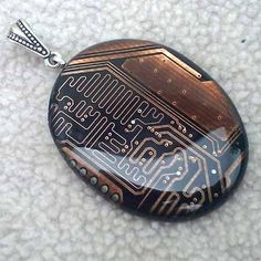 an electronic circuit board pendant on a silver chain with a black and gold pattern in the middle