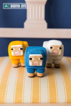 three small knitted sheep sitting on top of a yellow and white striped cushion in front of a blue wall