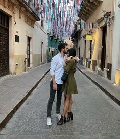 a man and woman standing in an alleyway with flags hanging from the buildings behind them