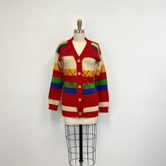 "Vintage 70s cardigan sweater featuring; a v neck long sleeves buttons down the front with wooden buttons with a longer cut in a horizontal stripe with a zig zag pattern stitched on the front ribbed at the neckline, cuffs, and hem of a mid weight, acrylic knit in primary colors of red, yellow, green, royal blue and off white labeled \"Knitmakers\" and tagged a size small, measurements when laid out flat are; 16 1/2 inches from pit to pit 19 3/4 inches sleeves 16 inches at the waist 13 1/2 inches Retro Button-up Cardigan For Fall, Retro V-neck Cardigan For Fall, Retro V-neck Winter Outerwear, Retro Winter Cardigan With Buttons, Retro Winter Cardigan With Button Closure, Retro Button-up Cardigan, Retro Multicolor Cardigan With Buttons, Multicolor Retro Cardigan With Buttons, Retro Multicolor Knit Outerwear