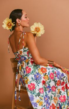 a woman sitting on a chair with flowers in her hair and wearing a floral dress