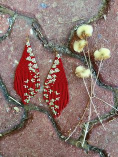 two pairs of red beaded earrings sitting on top of a stone floor next to dry grass