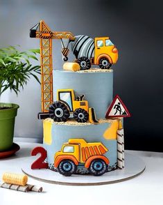 a three tiered cake with construction vehicles on it's side and a potted plant in the background