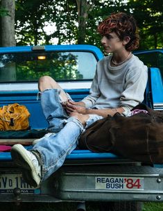 two people sitting in the back of a pick up truck with clothes on the bed