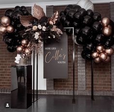 there is a black and gold balloon arch with flowers on the front, along with balloons in the back