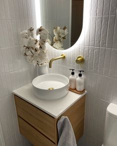 a white sink sitting under a bathroom mirror next to a wooden cabinet with a gold faucet