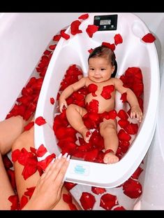 a baby sitting in a bathtub filled with rose petals and being held up by someone's hand