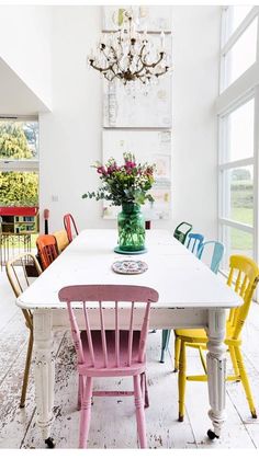 a dining room table with colorful chairs and a chandelier hanging from the ceiling