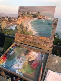 an artist's easel sitting on top of a wooden table next to the ocean