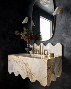 a bathroom sink with marble counter top next to a large mirror and flower vase on the wall