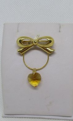 Never Worn Vintage Trifari gold-tone metal bow wire hanger yellow faceted crystal heart pendant charm holder badge hanger eyeglass holder ID tag holder with a standard C clasp. The wire hanger allows you to slide additional charms onto it. The bow is hallmarked Trifari. Length including bow hanger section & crystal heart 1 & 1/2 inches. Width of bow 1 & 1/8 inches. Width across of wire hanger 3/4 inch. Heart length 7/16 inch. Heart width 7/16 inch. I offer multiple-item-order shipping discounts. Yellow Gold Pendant Brooches As Gift, Yellow Brooch Jewelry For Wedding, Yellow Wedding Jewelry Brooch, Heart-shaped Brooch Jewelry Gift, Gold Heart-shaped Brooches For Gifts, Gold Heart Brooches For Wedding, Gold Round Brooches For Gifts, Valentine's Day Gold Jewelry Brooch, Valentine's Day Gold Brooch Jewelry