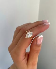 a woman's hand with a diamond ring on top of her finger and white nails