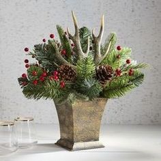 a vase filled with pine cones and red berries sitting on top of a white table