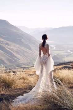 a woman standing on top of a grass covered hillside wearing a dress with an open back