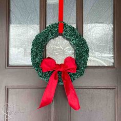 a green wreath with red bow hanging on the front door to give it a festive touch