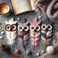 three knitted owls sitting on top of a table next to an open book and candle