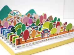 an image of a colorful card with trees and houses on the front, and a ferris wheel in the back