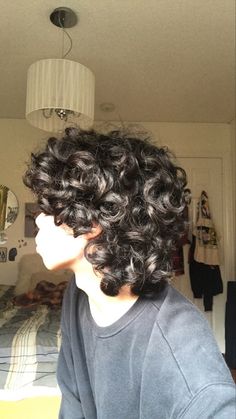 a woman with curly hair standing in front of a bed looking off into the distance