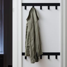 a coat hanging on the wall in front of a white door with black bars and hooks