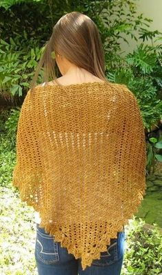 a woman wearing a yellow crochet shawl in front of some bushes and trees