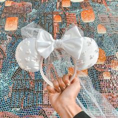 a hand holding a white bow on top of a mosaic wall