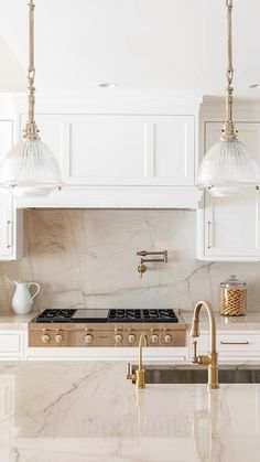 a kitchen with marble counter tops and white cabinets, two pendant lights over the stove