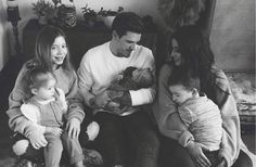 a black and white photo of a family sitting on a couch with their babys