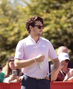 a man wearing sunglasses and holding a golf club in his hand while standing next to a red fence