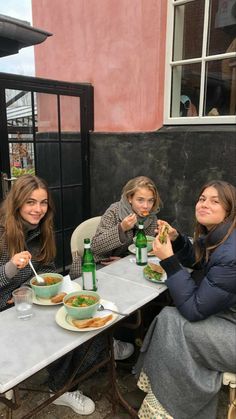 three women sitting at a table eating food and drinking green drinks in front of them