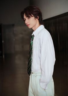 a young man wearing a white shirt and green tie standing in an empty room with his hands on his hips