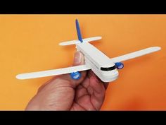 a hand holding a small white toy airplane on an orange background with blue wheels and propellers