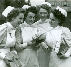 black and white photograph of women in nurses'uniforms holding medical supplies while smiling at the camera