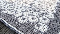 a crocheted rug with white and gray designs on it sitting on a wooden surface