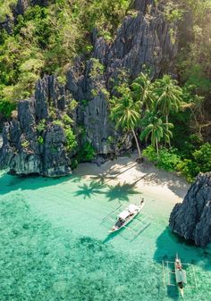 an aerial view of two boats in clear blue water next to rocky cliffs and palm trees