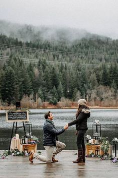 a man kneeling down next to a woman on a dock with flowers and trees in the background