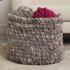 a large gray and red basket sitting on top of a rug next to a white couch