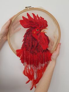 two hands are holding a red bird in a embroidery hoop with fringes on it