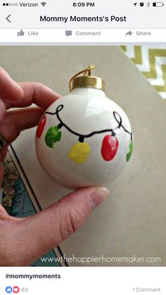 a hand holding a white ornament with christmas lights on it's side