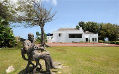 a statue of a man sitting on top of a bench in front of a house