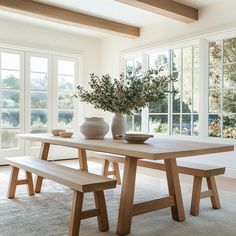 a wooden table with two vases on it and benches in front of the window