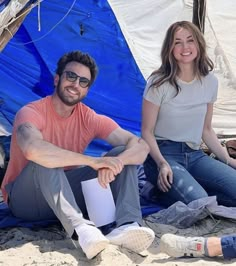 two people sitting on the ground in front of tents