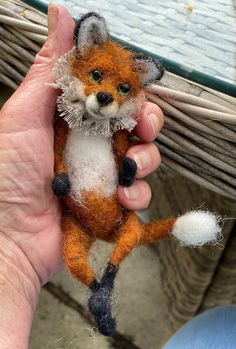 a hand holding an orange and white needle felt fox ornament on it's finger