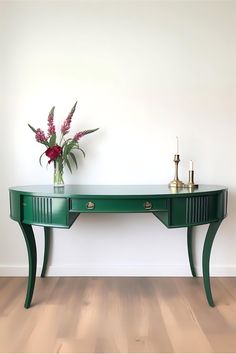 a green console table with flowers on top in front of a white wall and wooden floor