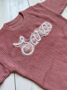 a pink sweater with the word baby written on it, sitting on a white wooden floor