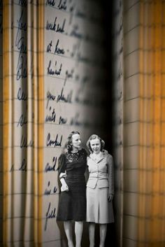 two women standing next to each other in front of a wall with writing on it